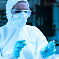 Scientist wearing a Hazmat suit, protection goggles and gloves holding a pipette and a petri dish